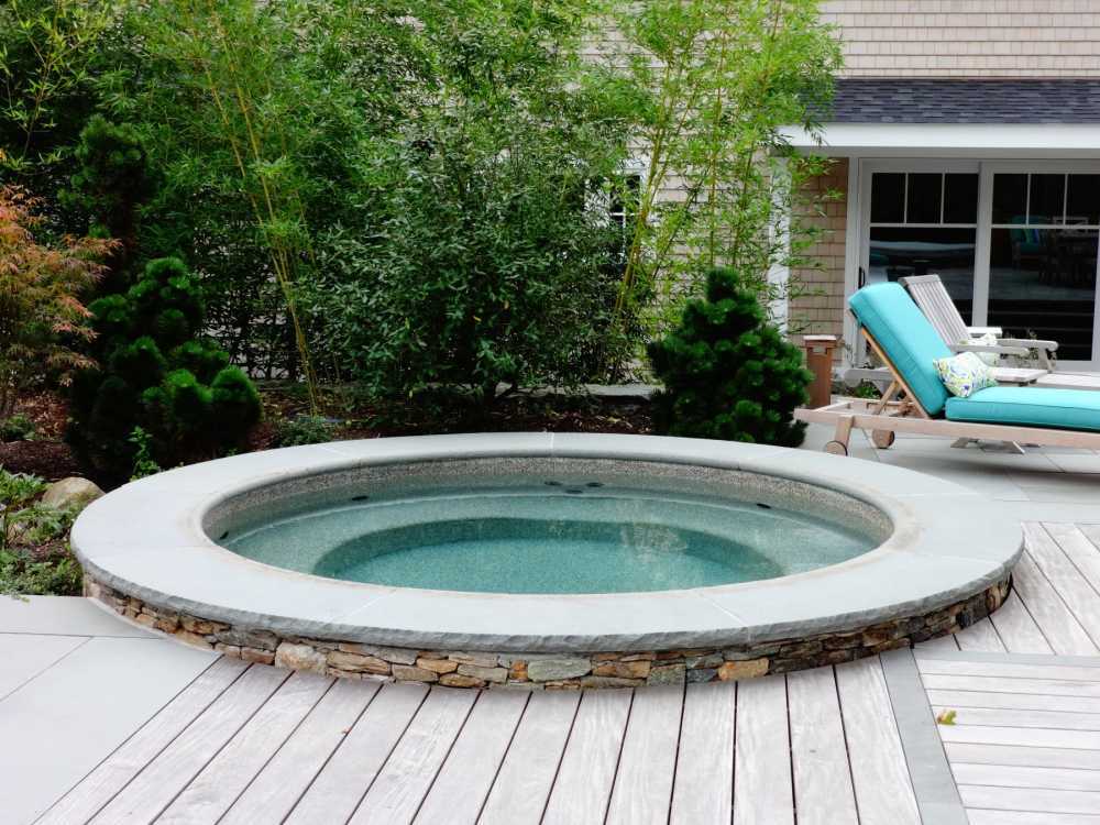 This hot tub is constructed of gunite, a sprayed in concrete, field stone veneer, and bluestone coping.  A garden of specimen trees and bamboo make a nice backdrop.